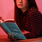 Woman in Red and Black Striped Long Sleeve Shirt Holding Blue Book