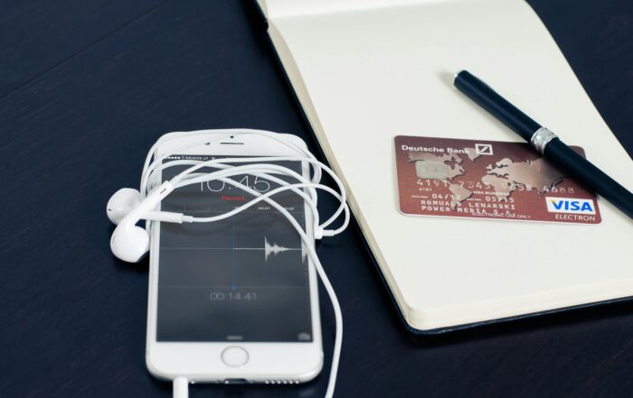 A white smartphone with earbuds, credit card, and pen on a notepad, symbolizing tech and finance.