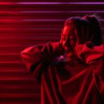 Woman with hands on head, expressing stress in neon red lighting.