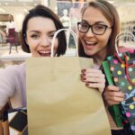 Two happy women holding shopping bags in a mall.