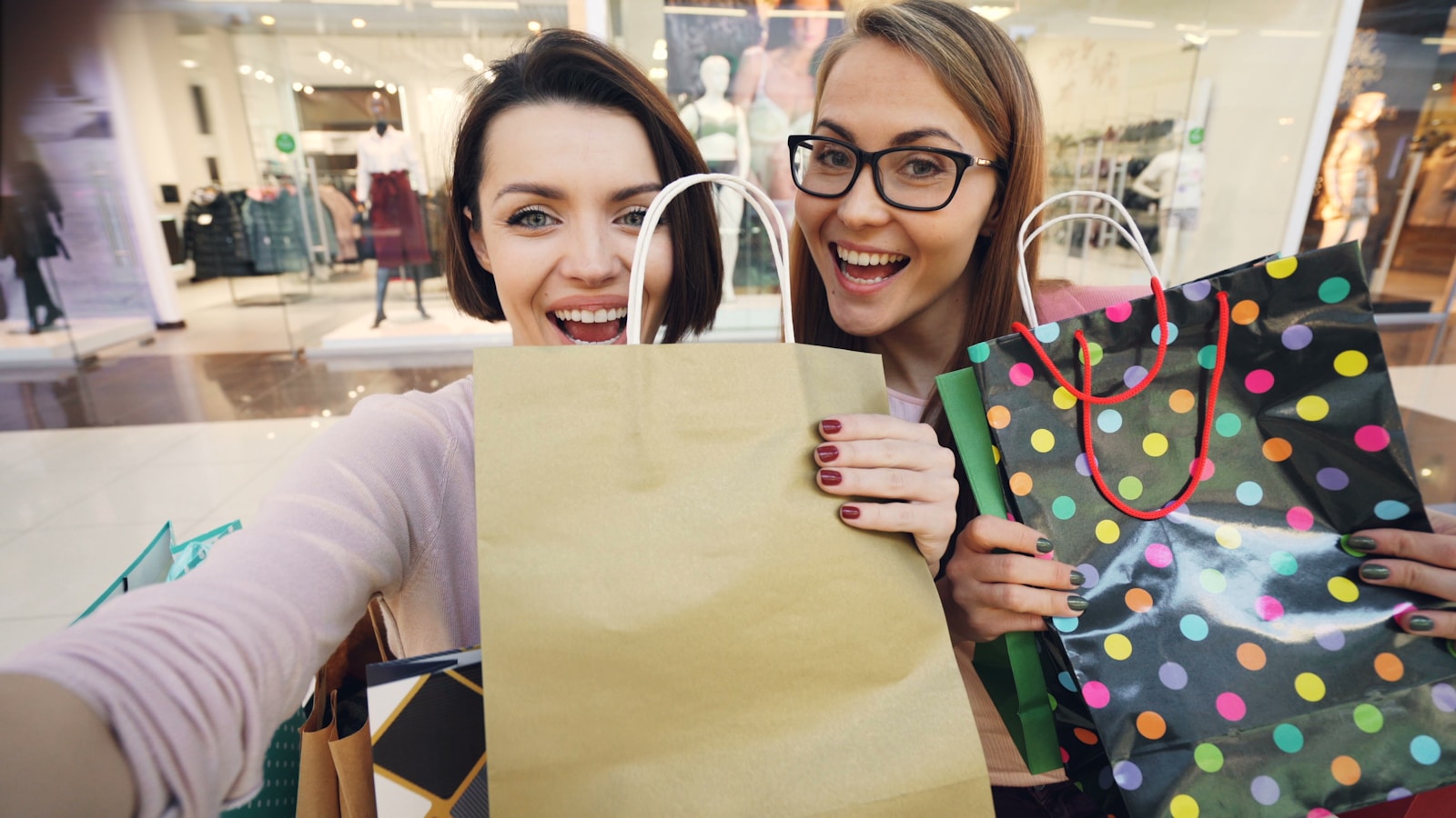 Two happy women holding shopping bags in a mall.
