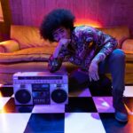 Retro-inspired fashion shoot featuring a person with afro hair posing with a vintage boombox indoors.