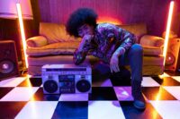 Retro-inspired fashion shoot featuring a person with afro hair posing with a vintage boombox indoors.