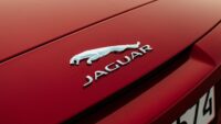 Detailed shot of Jaguar emblem on a red vehicle hood, emphasizing luxury.