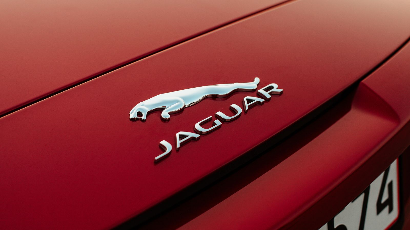 Photo by Sebastian Pichard Detailed shot of Jaguar emblem on a red vehicle hood, emphasizing luxury.