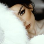 Close-up of a bride's face partially hidden by a feather fan, exuding elegance and mystery.