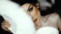 Close-up of a bride's face partially hidden by a feather fan, exuding elegance and mystery.