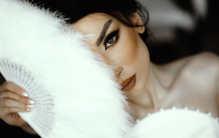 Close-up of a bride's face partially hidden by a feather fan, exuding elegance and mystery.