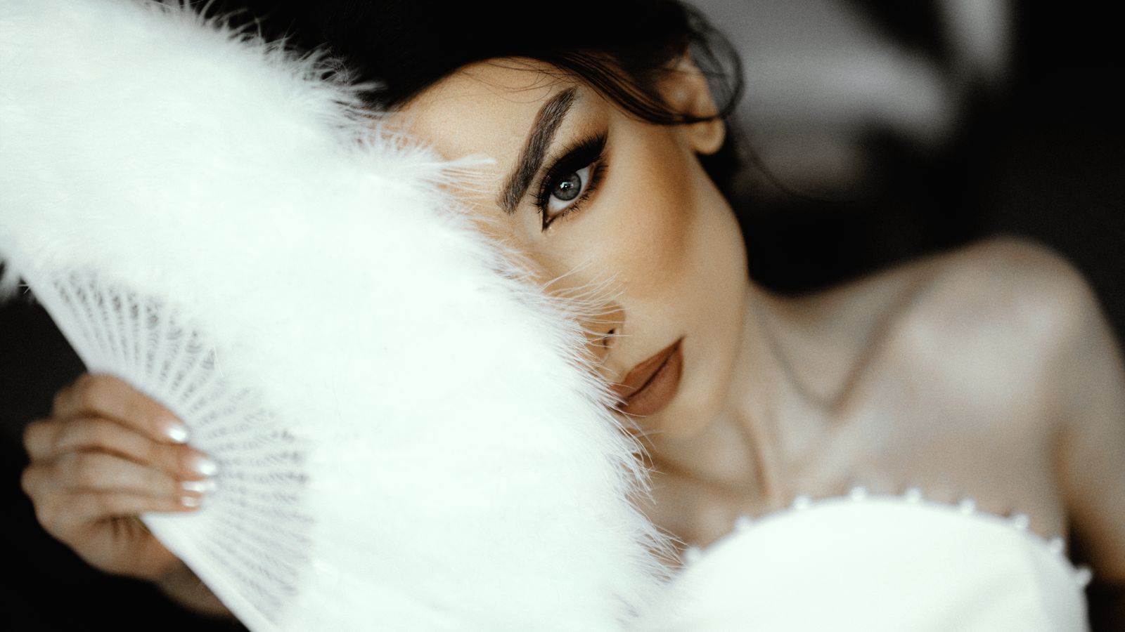 Photo by alirezamani wedding team Close-up of a bride's face partially hidden by a feather fan, exuding elegance and mystery.